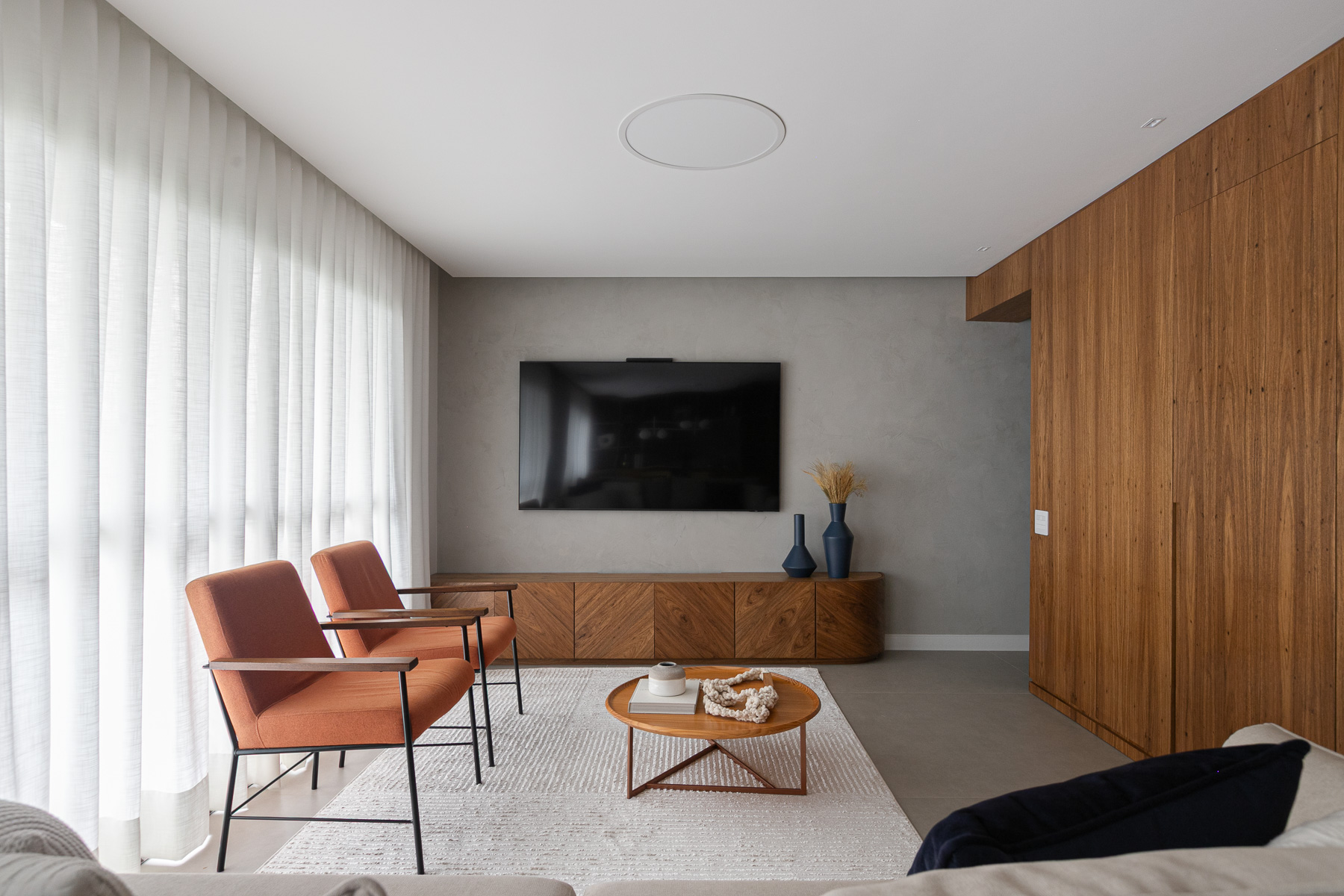 Sala de estar com poltronas em tom terracota e painel em marcenaria